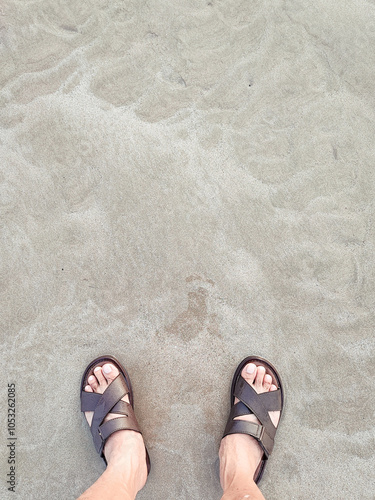 The foot standing on the sand beside the sea, close-up