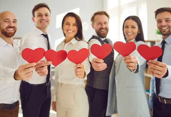 Group of business people stands in the office, holding red hearts. Love and togetherness, possibly in a volunteer or valentine day context, showcasing a diverse team united in purpose.