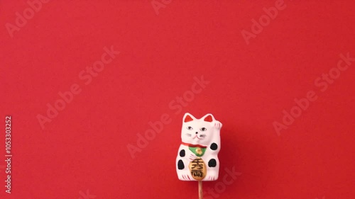 Maneki-neko moving on the red background. Maneki-neko is Japanese doll that brings good luck. 赤背景上を動く招き猫。招き猫は幸運をもたらす日本の人形	
