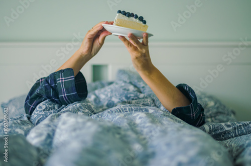 woman eating a Cheesecake in Pajamas for a Cozy Dessert Moment in bedroom photo