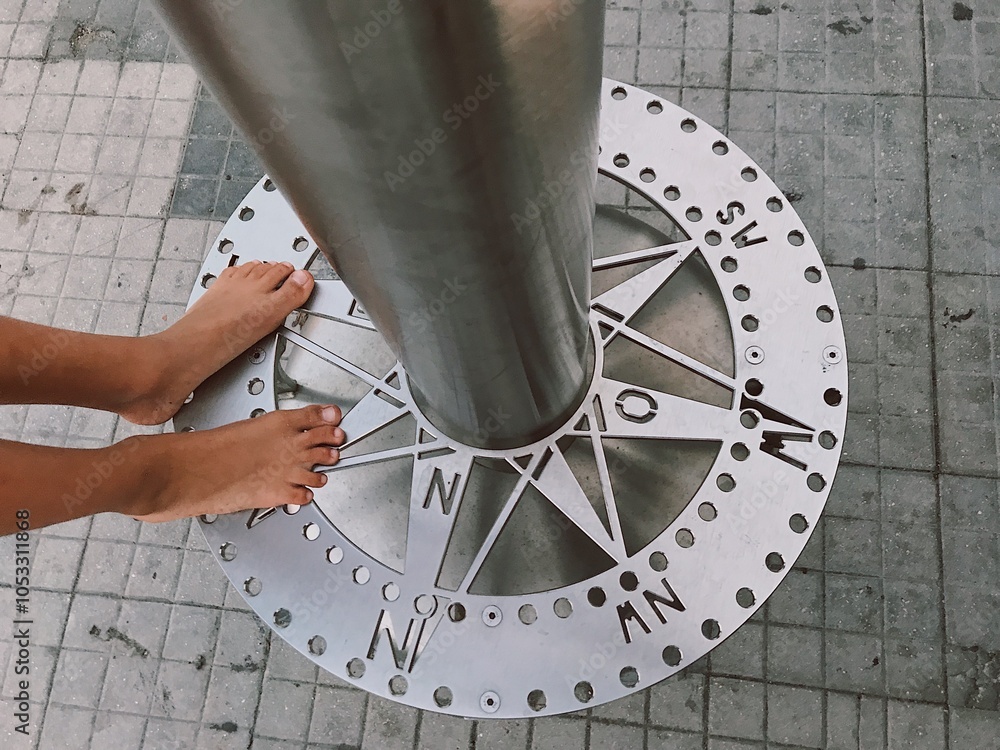 A persons feet are firmly standing on a large compass design that is placed on the ground beneath them, indicating directions A persons feet are firmly standing on a large compass design that is placed on the ground beneath them, indicating directions