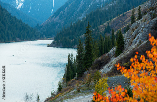 the tranquil splendor of a mountain lake cradled by forested slopes, with vibrant autumn foliage in the foreground and serene waters, the overcast sky, a crisp fall day photo