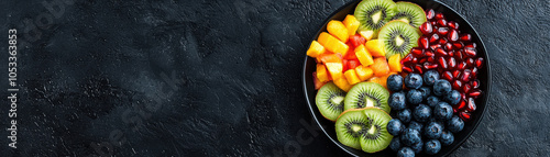 A vibrant bowl of assorted fresh fruits, including kiwi, blueberries, mango, and pomegranate, displayed on a dark textured background.