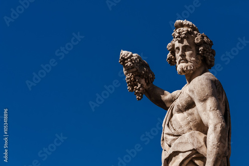 Paganism in Ancient Times. Roman or Greek god Bacchus holding grapes, a baroque statue, erected in the 17th century on Holy Trinity Bridge in Florence historic center (with blue sky and copy space)