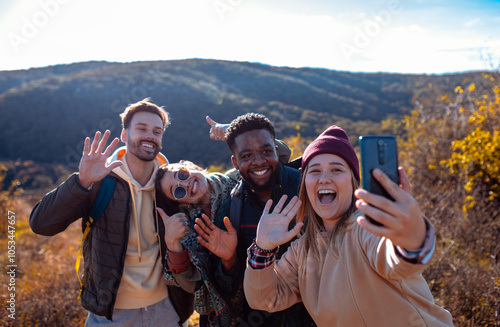 Smiling group of friends having fun while hiking together on hill at sunset and making selfie  with smart phone. photo