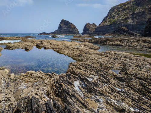 Rough stone that forms natural puddles at low tide along the cliff on Odeceixe beach, PORTUGAL photo