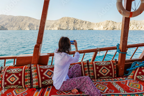 Canvastavla woman sitting on a tourist dhow boat, takes photos of cliffs and fjords by phone