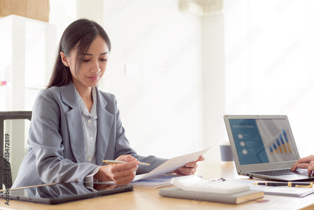 Female financier using laptop Make a report for a financial company, sit at a desk in the office to calculate tax expenses using a calculator and analyze financial documents. Female financier using laptop Make a report for a financial company, sit at a desk in the office to calculate tax expenses using a calculator and analyze financial documents.