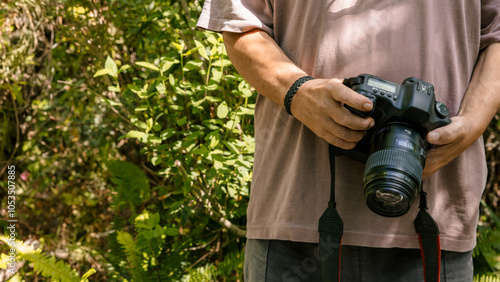Fotografie Unrecognizable man holding professional camera in a lush green outdoor setting