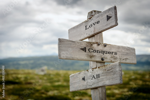 love conquers all text quote written on wooden signpost at the crossroads outdoors in nature. photo