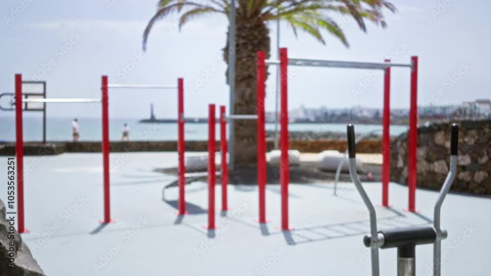 Outdoor calisthenics park with red workout equipment and a defocused man walking near the ocean, framed by a palm tree and scenic coastal view. Outdoor calisthenics park with red workout equipment and a defocused man walking near the ocean, framed by a palm tree and scenic coastal view.