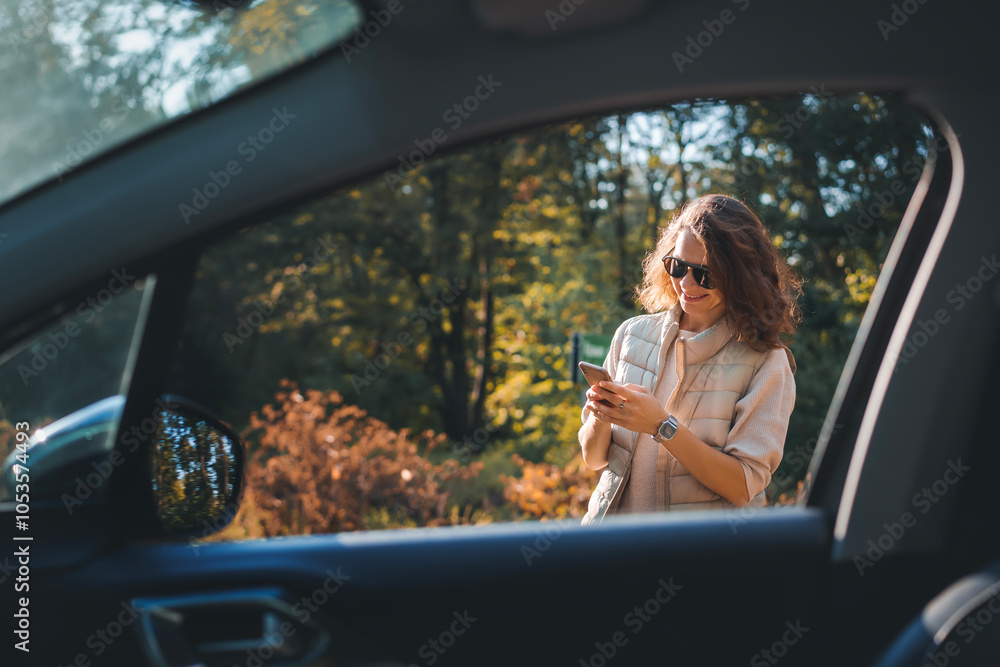 Happy woman driver traveling by car in forest enjoying freedom and nature, using smartphone
