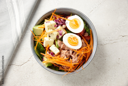 A bowl of tuna salad topped with boiled egg and cubed cheese photo