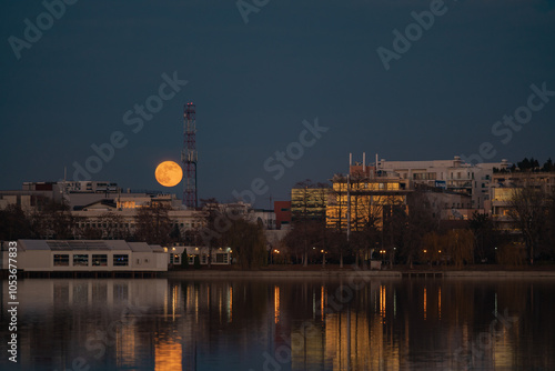 Amazing urban landscape with tall buildings illuminated at night and reflected in the water. Moonrise above the skyscrapers of Bucharest, the capital of Romania