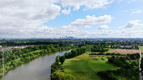 Drone video of Frankfurt's skyline on a partly cloudy day, featuring the Main River in the foreground and adjacent fields. Drone move right