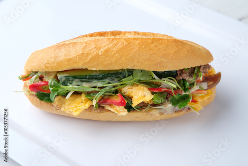 Bahn mi filled with fresh herbs and vegetables served on a white plate. photo