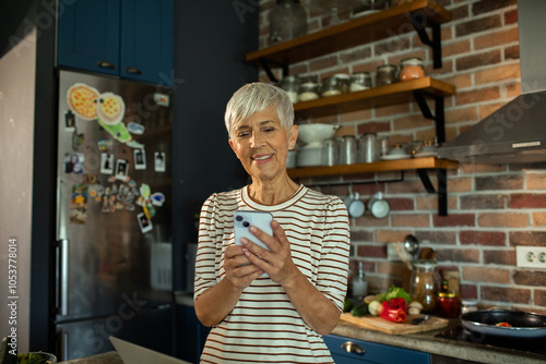 Smiling senior woman using smartphone in modern kitchen