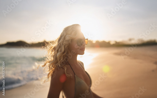 A woman with long, blonde hair walks along a sandy beach with the setting sun in the background.