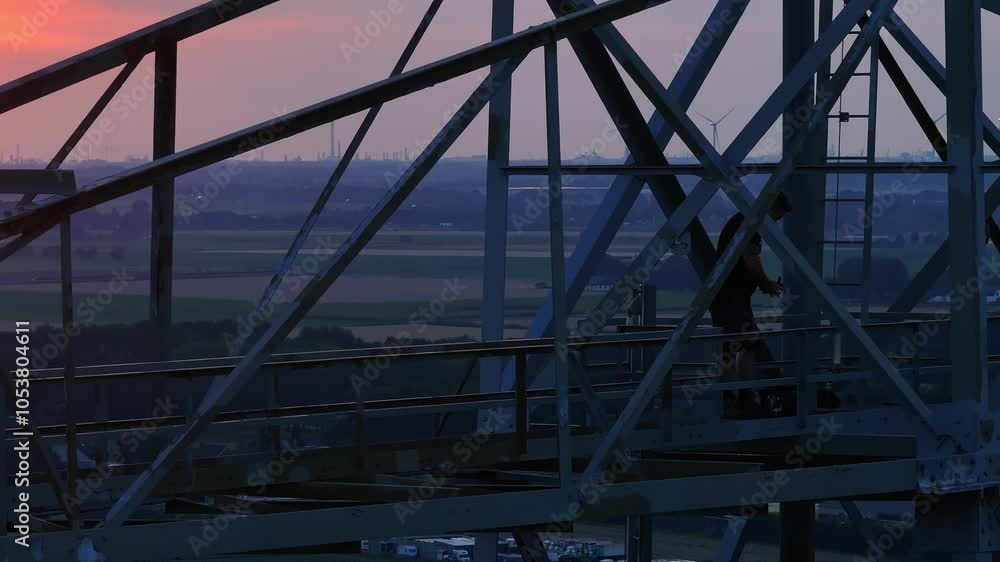Man standing on a metal structure at sunset with a wide landscape in the background Man standing on a metal structure at sunset with a wide landscape in the background