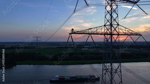 Man working high above a river on an electrical transmission tower during sunset