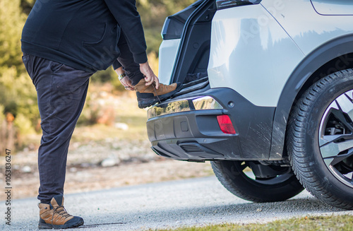 Person about to tie his hiker boots on his car in the mountain, packed for an outdoor adventure.