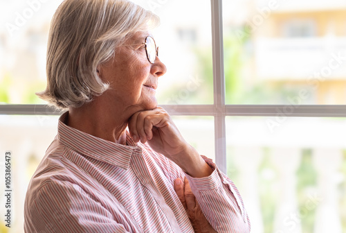 Portrait of pensive senior woman at home looking out the window lost in her thoughts photo