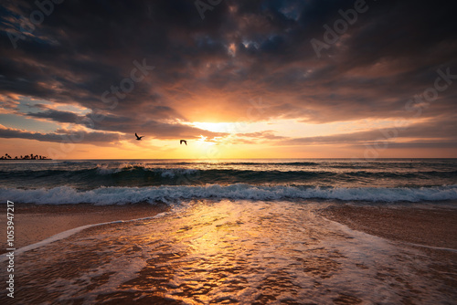 Scenic sunrise over the sea waves and beach with dramatic clouds and sun rays