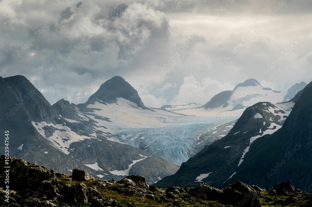 Obraz premium Dramatic sunset over the Swiss Alps with clouds casting soft, muted tones on rugged peaks