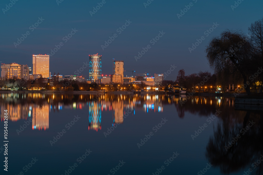 Obraz premium The lake in the Herastrau park at dusk. Night landscape with Skyscrapers with lit lights reflecting in the water at night