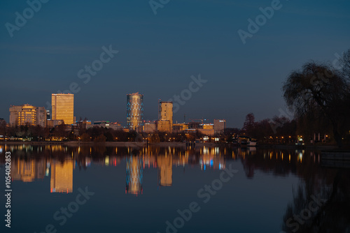 The lake in the Herastrau park at dusk. Night landscape with Skyscrapers with lit lights reflecting in the water at night