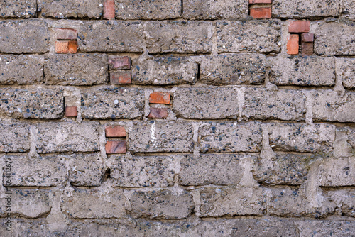 A brick wall with a few bricks missing. The wall is grey and has a rough texture. The missing bricks give the wall a sense of decay and abandonment