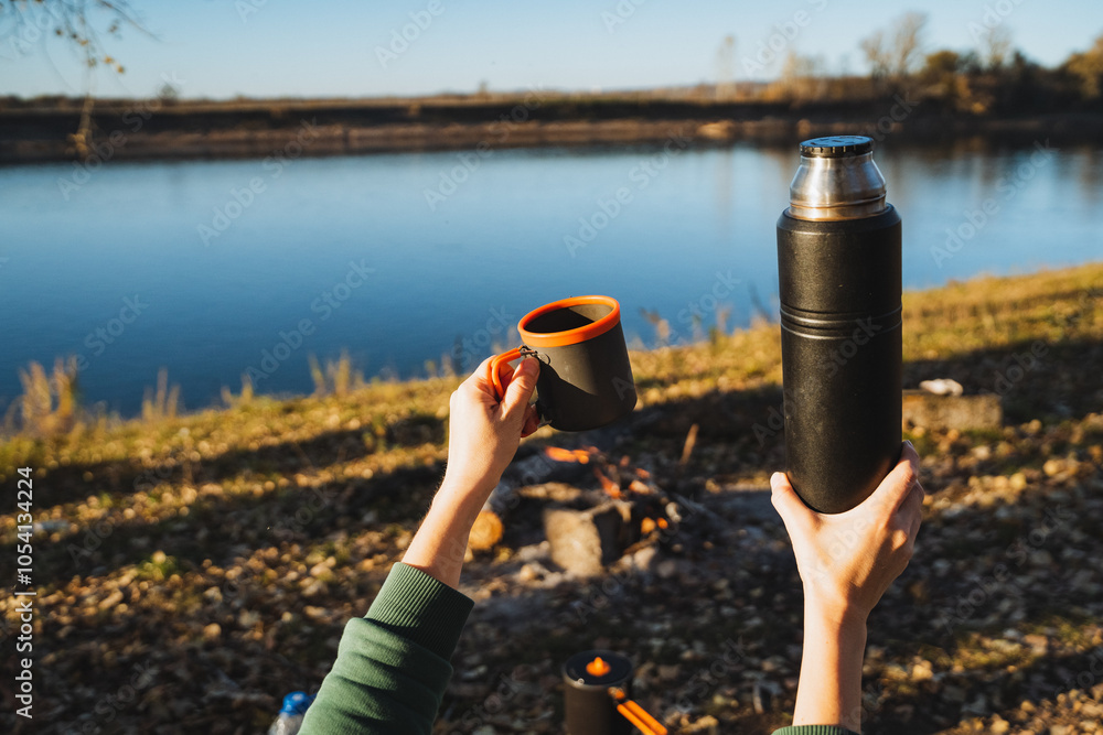 Obraz premium Taking pleasure in a warm and delicious beverage while sitting by the beautiful river a memorable outdoor adventure moment to cherish