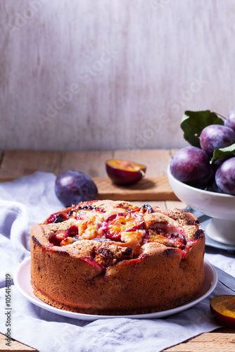 Obraz na płótnie Plum pie with filling and sugar crust, sprinkled with powdered sugar and plums on a wooden table. w salonie