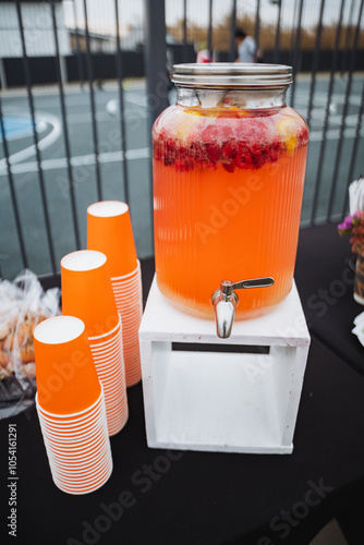 Enjoy a delightful refreshing fruitinfused beverage dispenser accompanied by colorful cups at your next outdoor gathering or celebration event photo