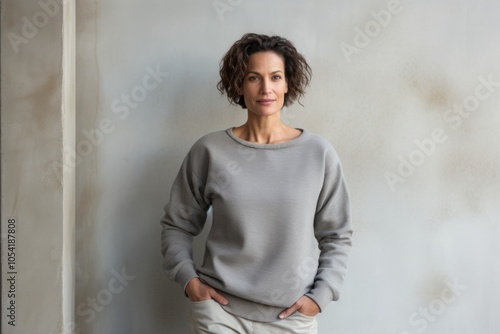 Portrait of a content woman in her 40s wearing a thermal fleece pullover over bare concrete or plaster wall