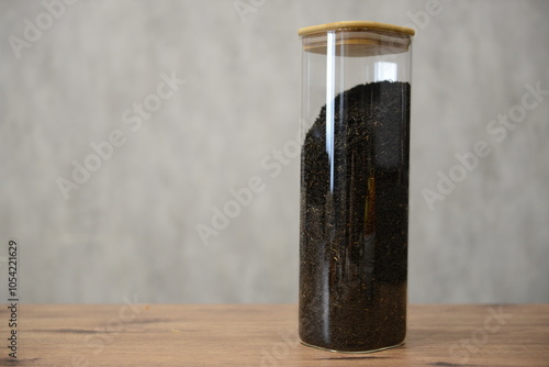 A clear glass container filled with black tea mixture sitting on a wooden table against a light textured background