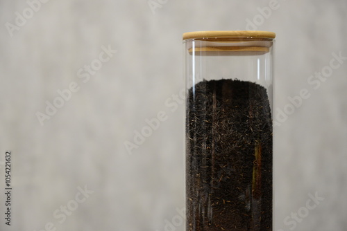 A clear glass container filled with black tea mixture sitting on a wooden table against a light textured background