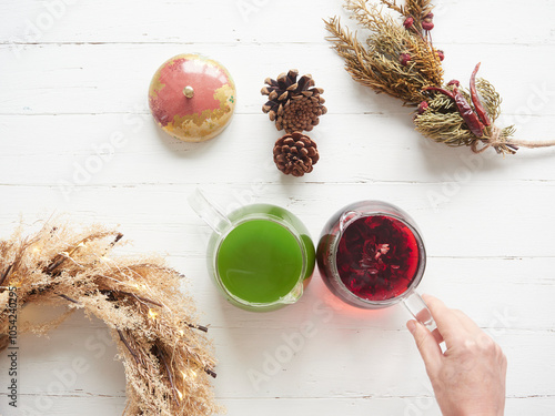 Top view of a hand reaching for red and green tea with natural holiday decorations on a wooden table