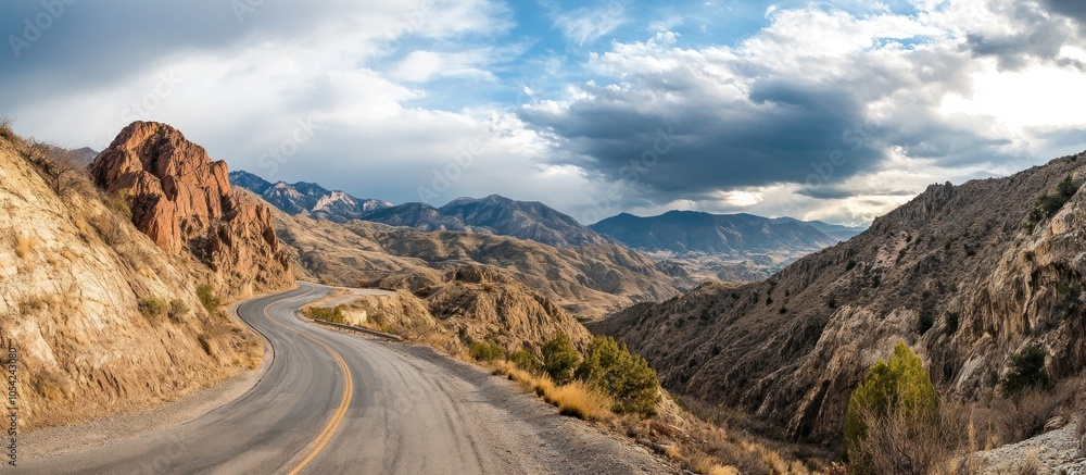 Fototapeta premium Winding road through mountains with dramatic clouds overhead.