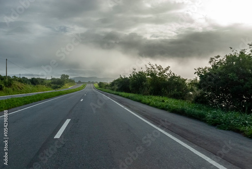 Paved dual-lane highway in perspective, with no cars, early in the morning, with a bit of fog and lush green landscape in the background in Brazil. photo