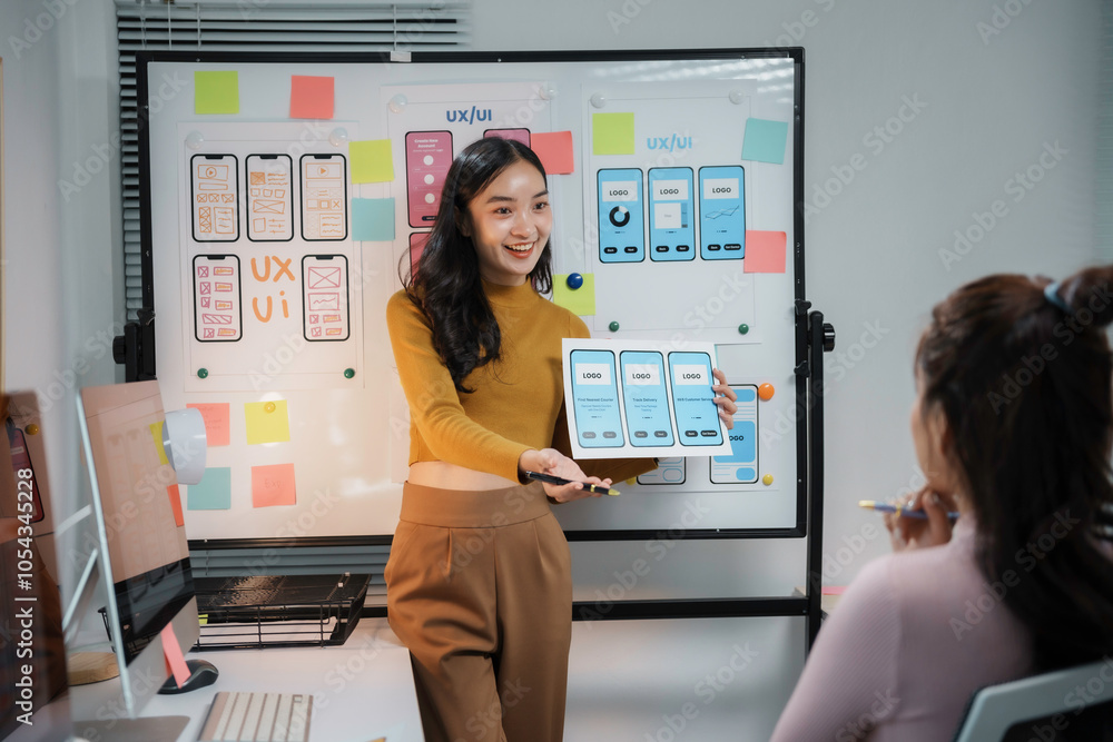 Asian women working together developing user interface of mobile application using wireframe and sticky notes Asian women working together developing user interface of mobile application using wireframe and sticky notes