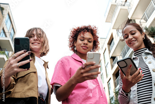 Three young women are using mobile phones while walking in the city photo