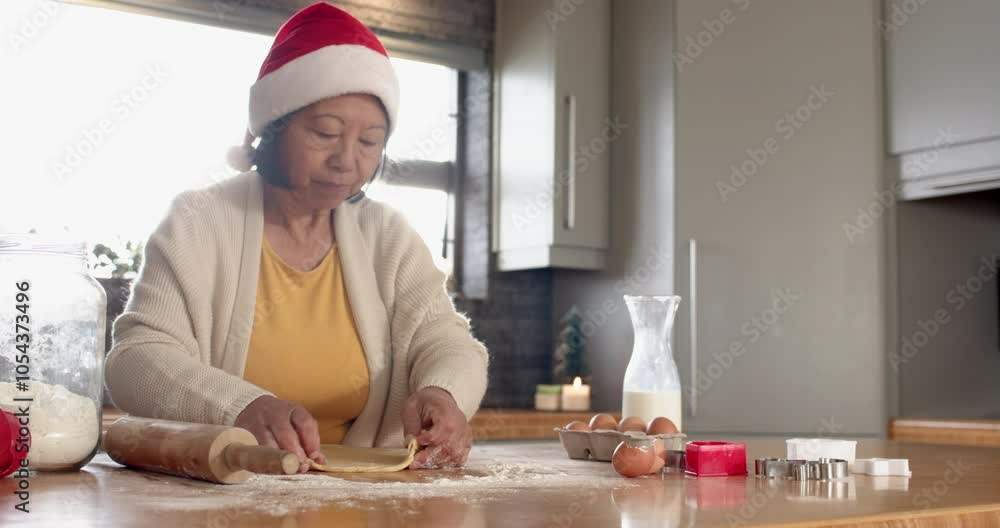 Senior Asian woman in Santa hat baking Christmas cookies at home, feeling joyful Senior Asian woman in Santa hat baking Christmas cookies at home, feeling joyful