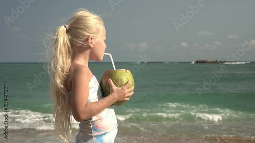 Child girl drinking juice from green coconut on sea beach