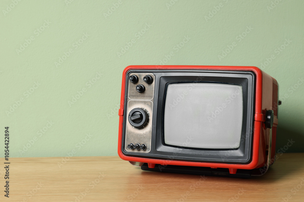 Obraz premium Retro tv set on wooden shelf against green wall. Space for text