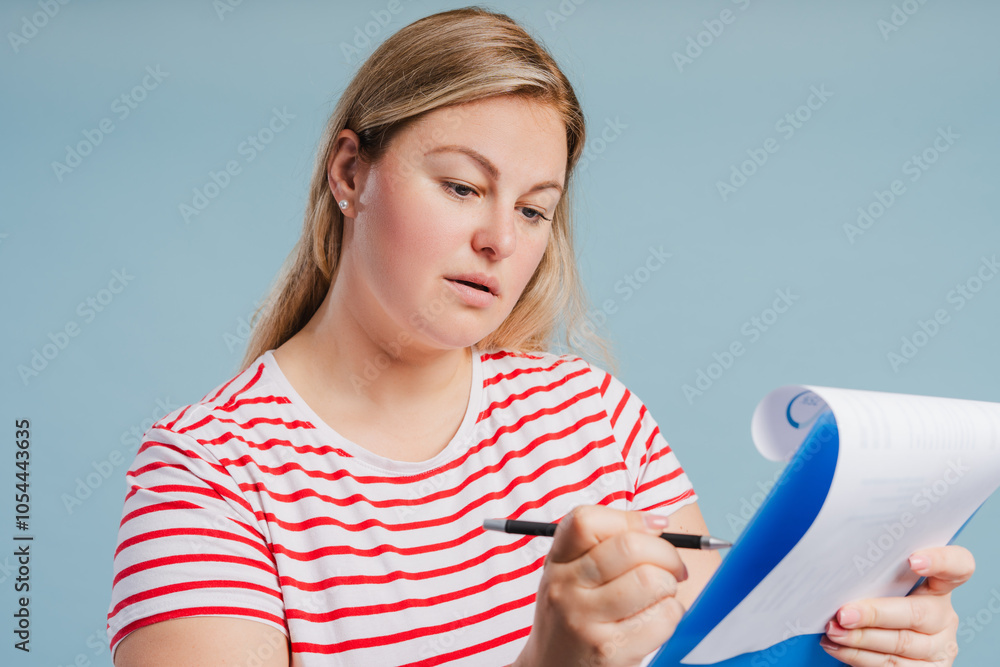 Young plus size woman making notes posing in studio over blue background Young plus size woman making notes posing in studio over blue background