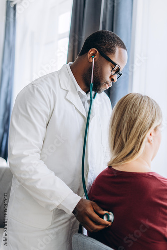 African American doctor examining with stethoscope young woman in clinic