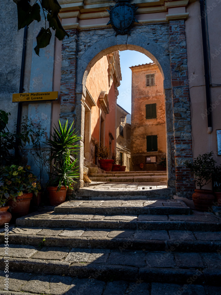 Fototapeta premium Torbogen in der historischen Altstadt von Marciana, Elba, mit Sonnenstrahlen, die durch den Bogen scheinen – Mediterraner Charme und antike Architektur