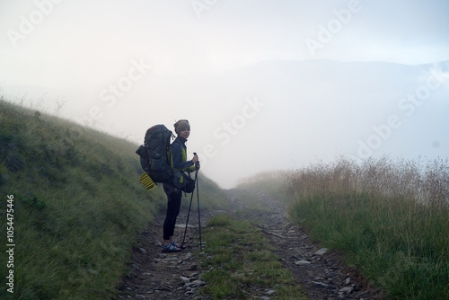 A young girl travels, is engaged in active sports, climbs with trekking poles in atmospheric weather, the slopes of the mountains and the forest