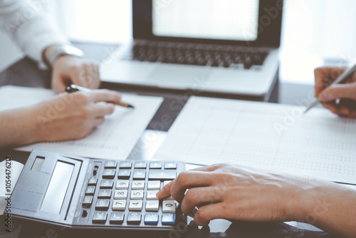 Two accountants use a calculator and laptop computer for counting taxes or revenue balance. Business, audit, and taxes concepts photo